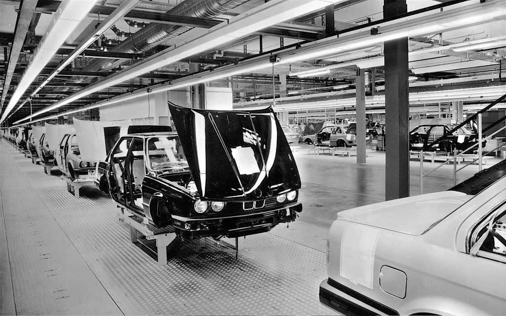 Photograph shows early-model E30 in production on factory floor.